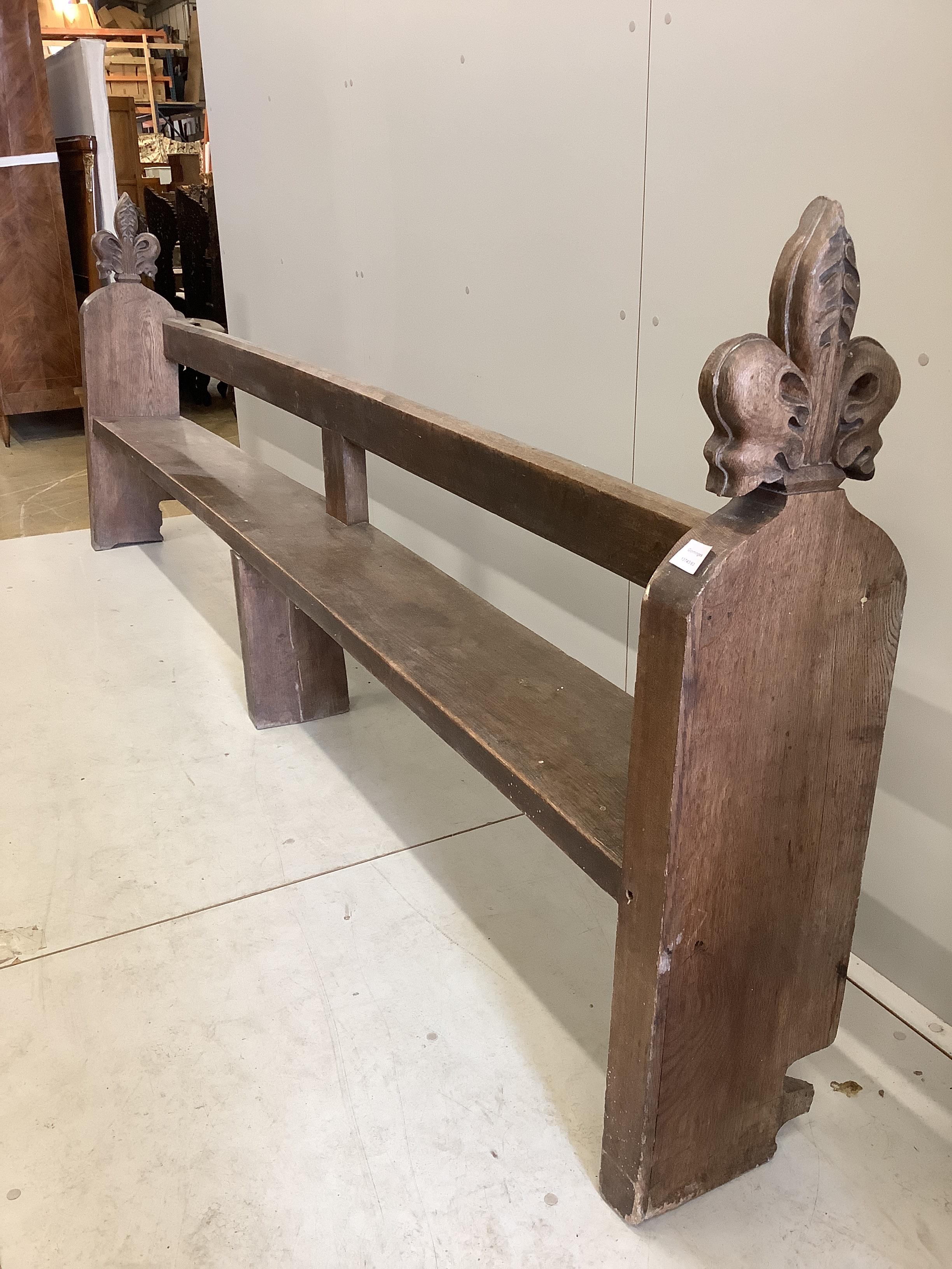 An oak pew with carved fleur de lys finials, width 304cm, depth 28cm, height 108cm